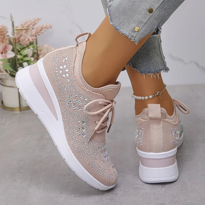 Light pink orthopedic sneakers with shiny details, worn with jeans, set in a minimalistic indoor space.