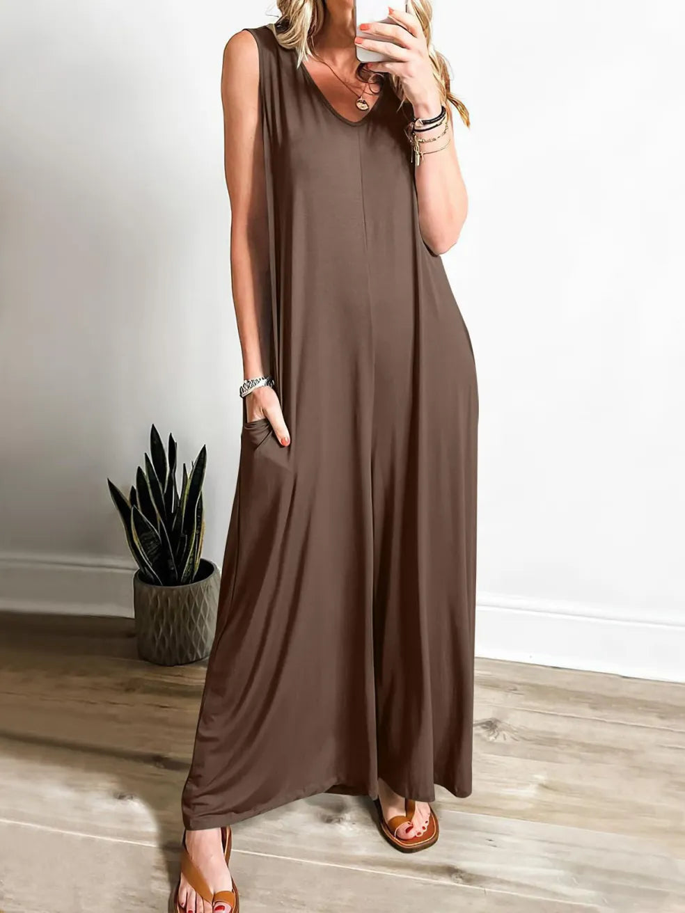 Brown V-neck jumpsuit with wide legs, modeled indoors with a plant in the corner.