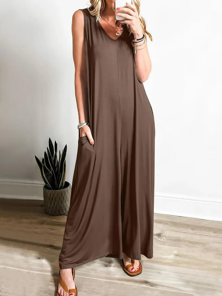 Brown V-neck jumpsuit with wide legs, modeled indoors with a plant in the corner.