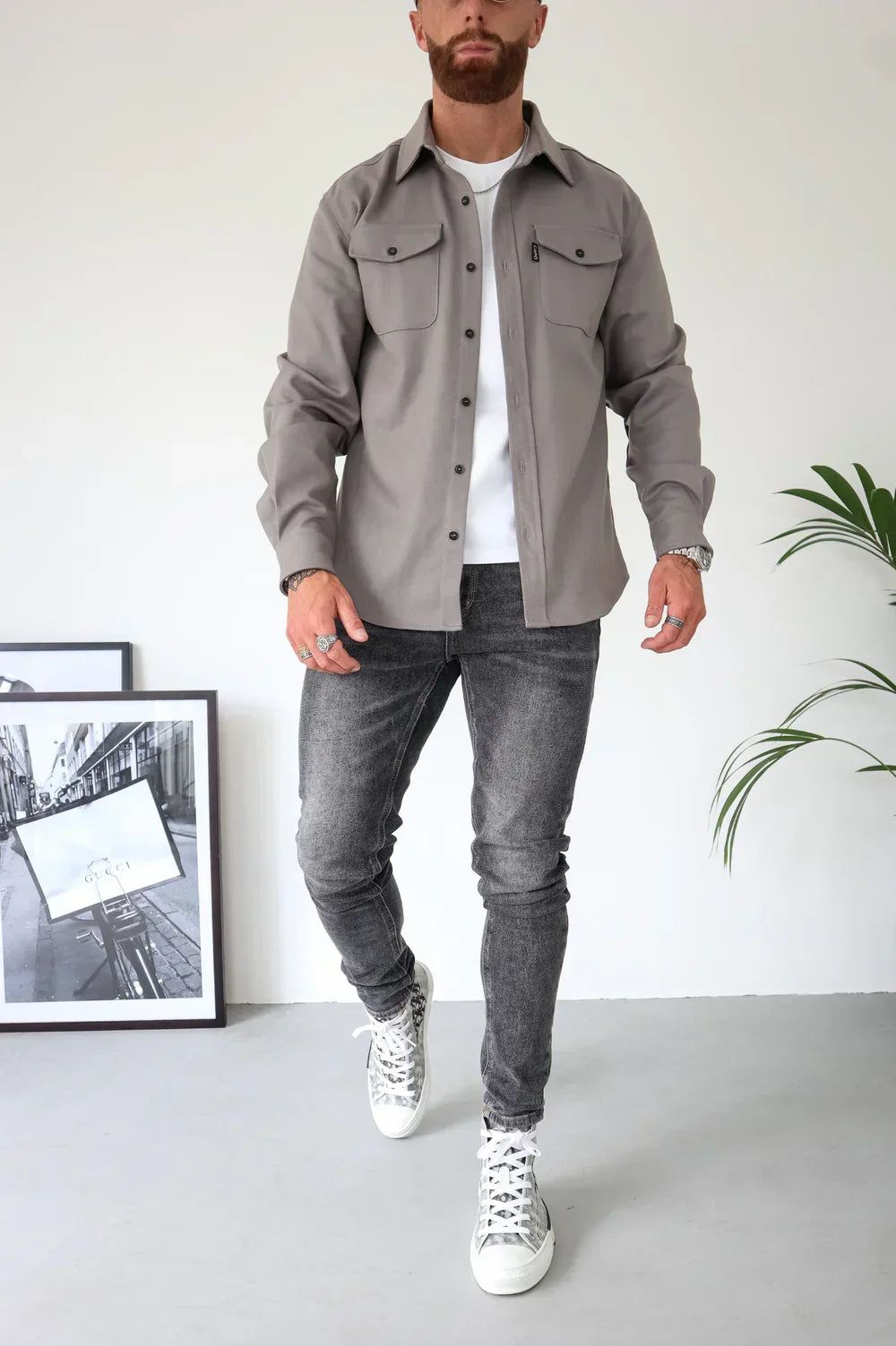 Beige overshirt over white t-shirt, paired with grey jeans and sneakers, standing indoors.
