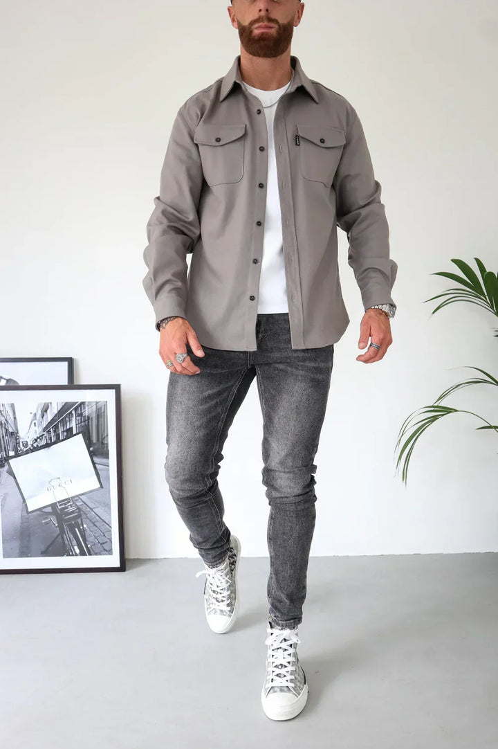 Beige overshirt over white t-shirt, paired with grey jeans and sneakers, standing indoors.