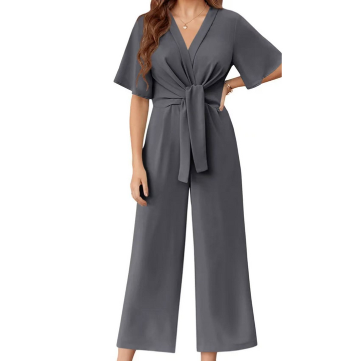 Gray elegant jumpsuit with short sleeves and a tie waist on a woman, studio background.