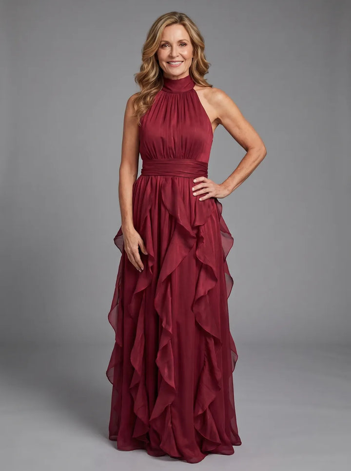 Model in a burgundy high neck maxi dress with gathered ruffle layers, set against a gray studio backdrop.