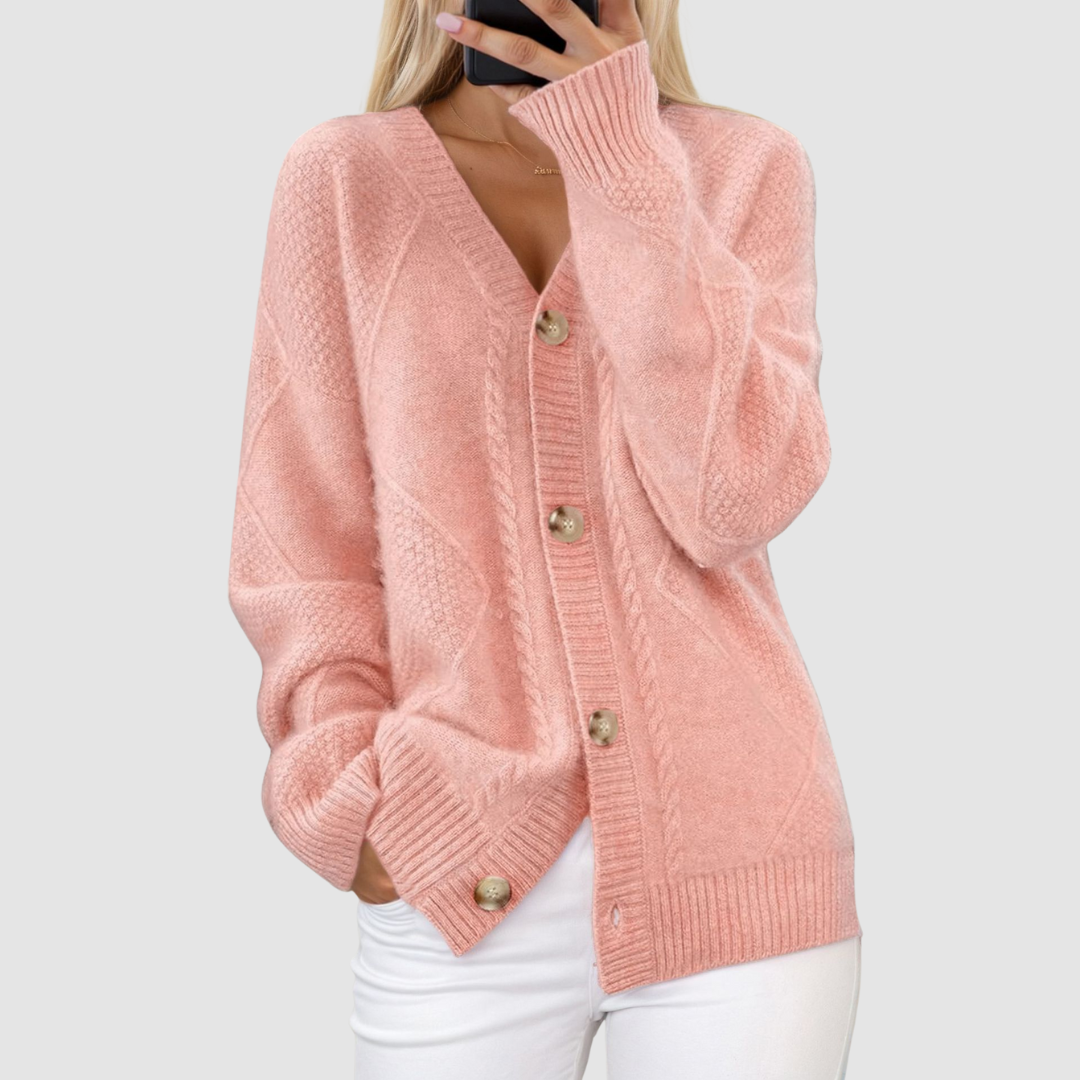 Pink knitted V-neck cardigan with button detailing, styled with a hand in pocket, set against a light gray background.