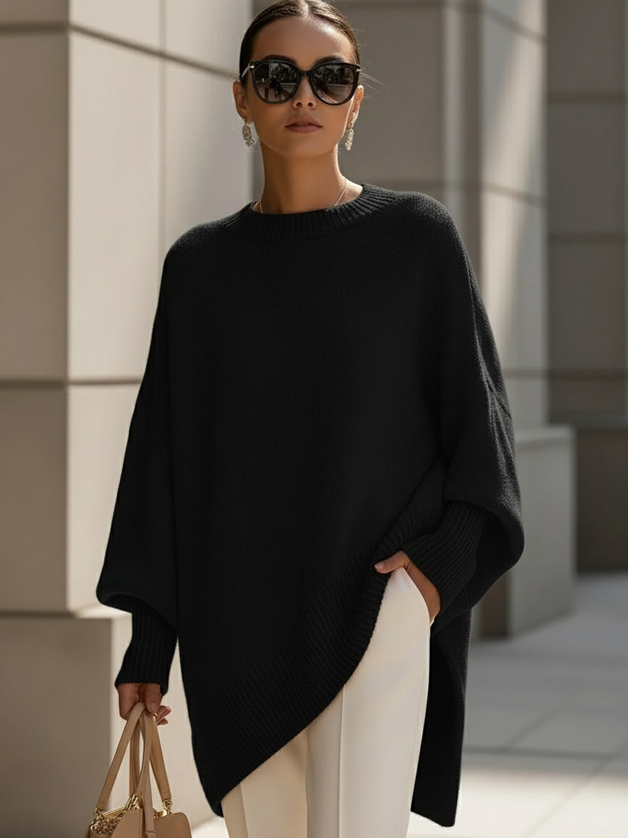 Woman in a loose black sweater with ribbed hem and cuffs, paired with white pants, in an urban setting.