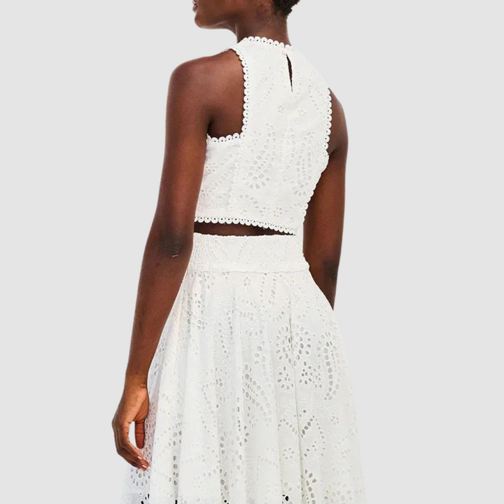 Back view of a white two-piece set with intricate cutout details, showing top and part of a skirt on a white background.