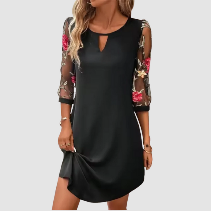 Black summer dress with floral print sheer sleeves, modeled indoors with a neutral background.