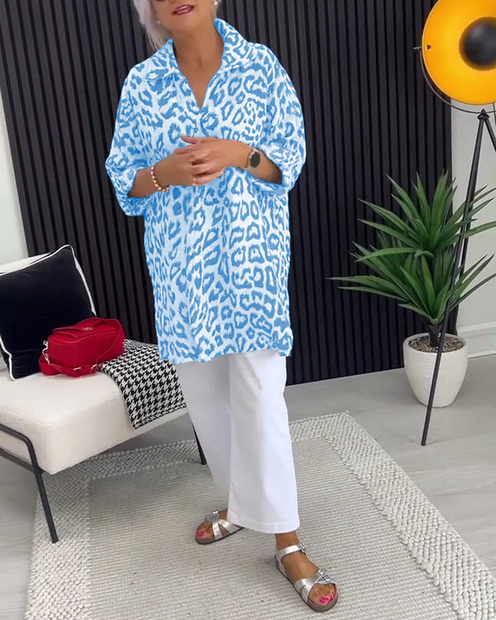 Blue leopard print blouse with structured collar, worn with white pants, in a fashionable indoor environment with decor.