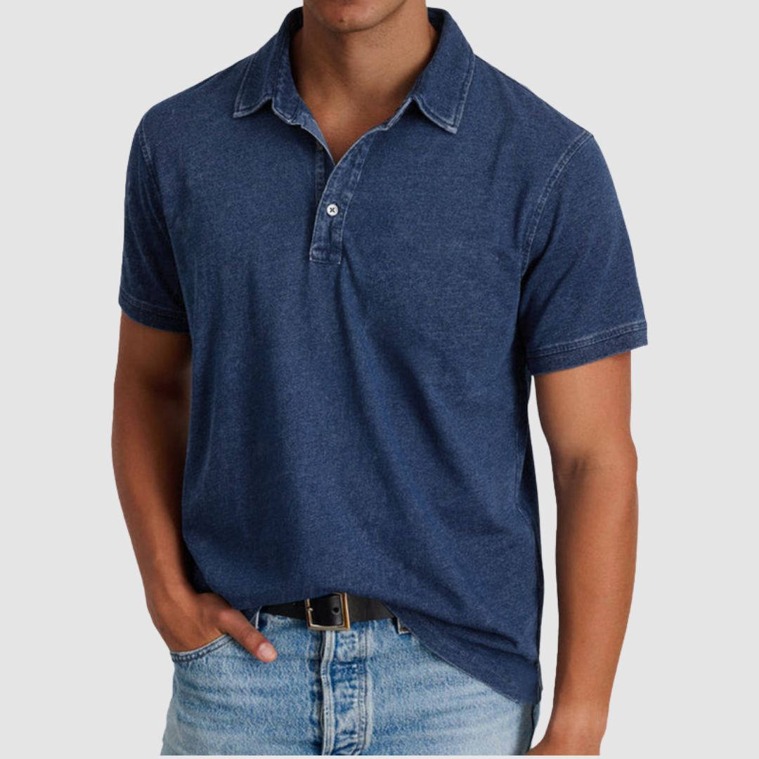 Man wearing a dark blue classic collared polo with short sleeves and button placket, paired with jeans in a studio environment.
