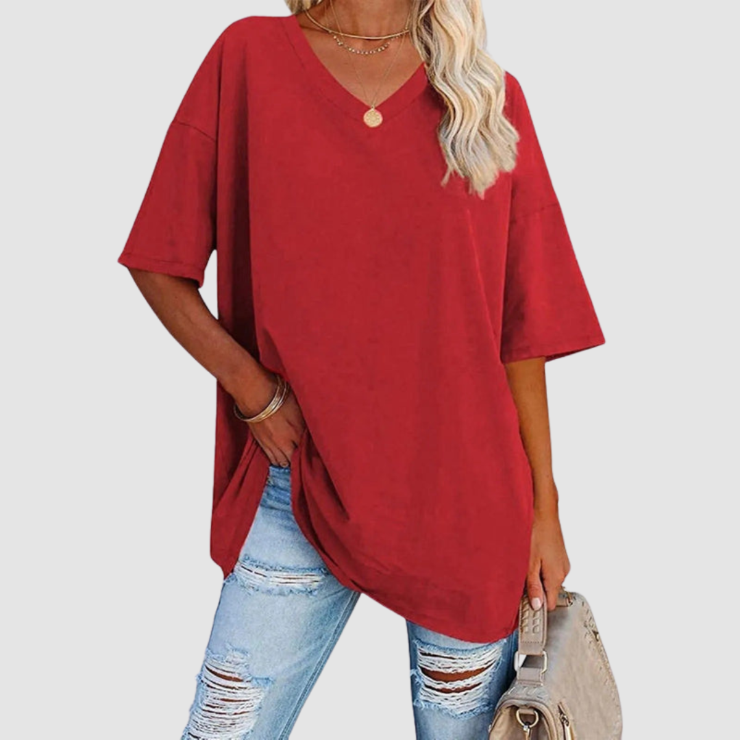 Woman in a red V-neck T-shirt with distressed jeans, holding a beige bag, studio background.