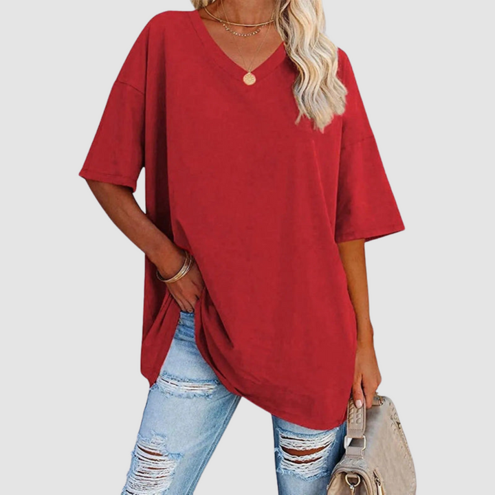 Woman in a red V-neck T-shirt with distressed jeans, holding a beige bag, studio background.