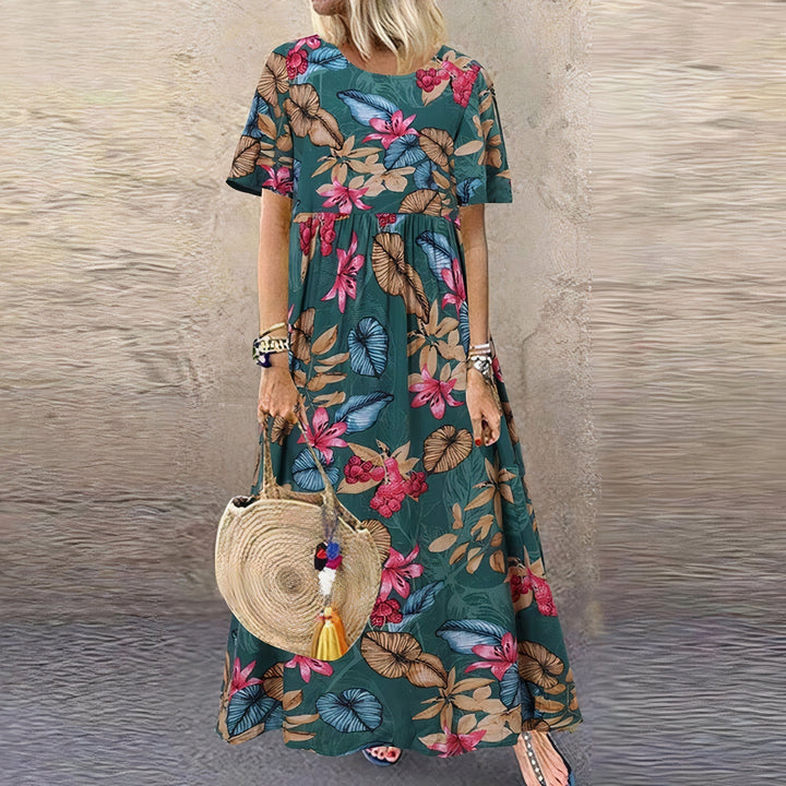 Model in a green floral dress with pink and blue leaf patterns, accessorized with a woven bag, textured wall backdrop.