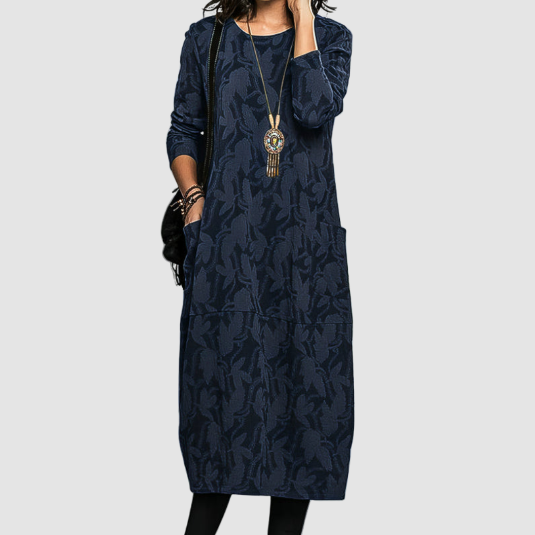 Woman in chic navy dress adorned with a nature-inspired pattern, accessorized with a statement necklace, isolated on a simple background.