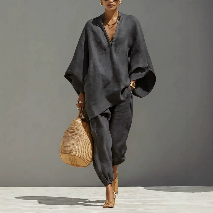 Model in dark grey batwing sleeve V-neck lounge set with woven bag, studio background.