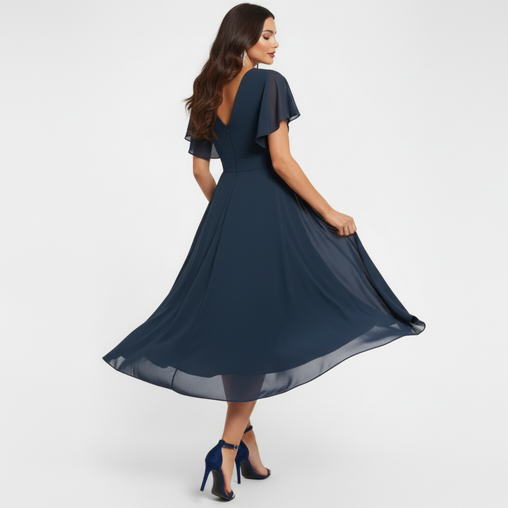 Side view of woman in navy flowing V-neck maxi dress, highlighting flared hem and short sleeves, in a studio setting.