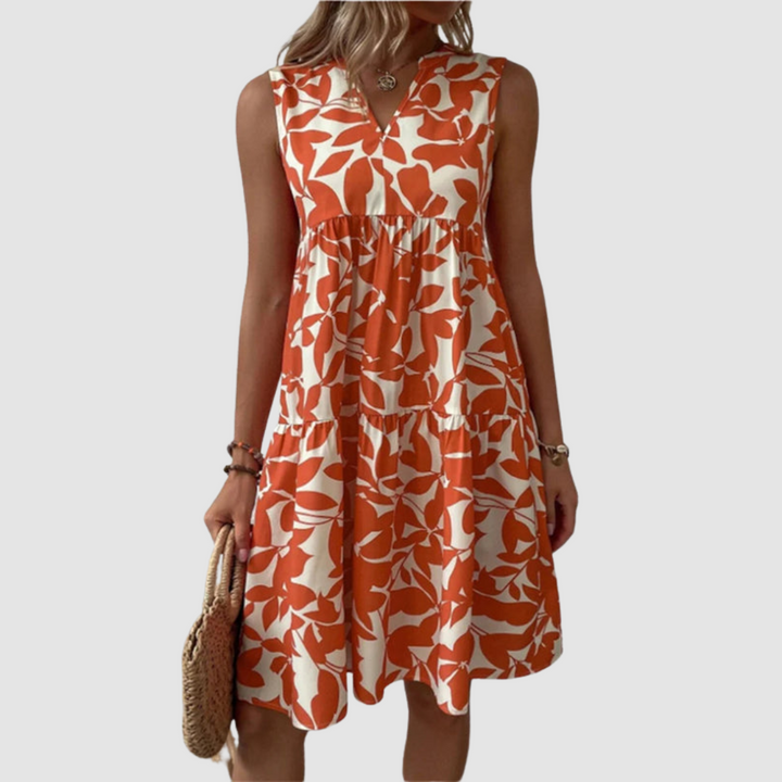 Model wearing a sleeveless orange and white floral print flowy dress, holding a woven bag, against a plain background.