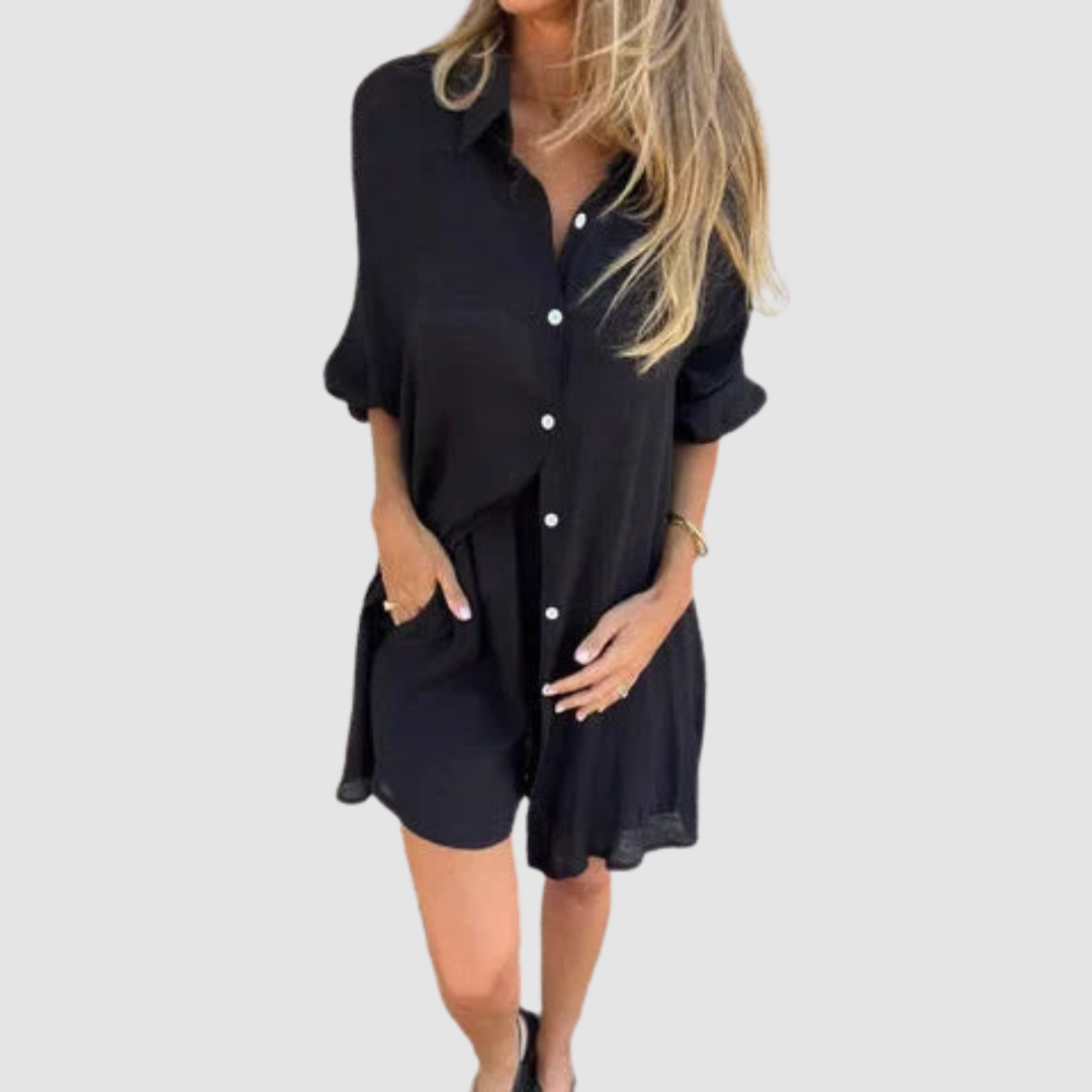 Model wearing a black two-piece set with button-up shirt and shorts; neutral studio background.