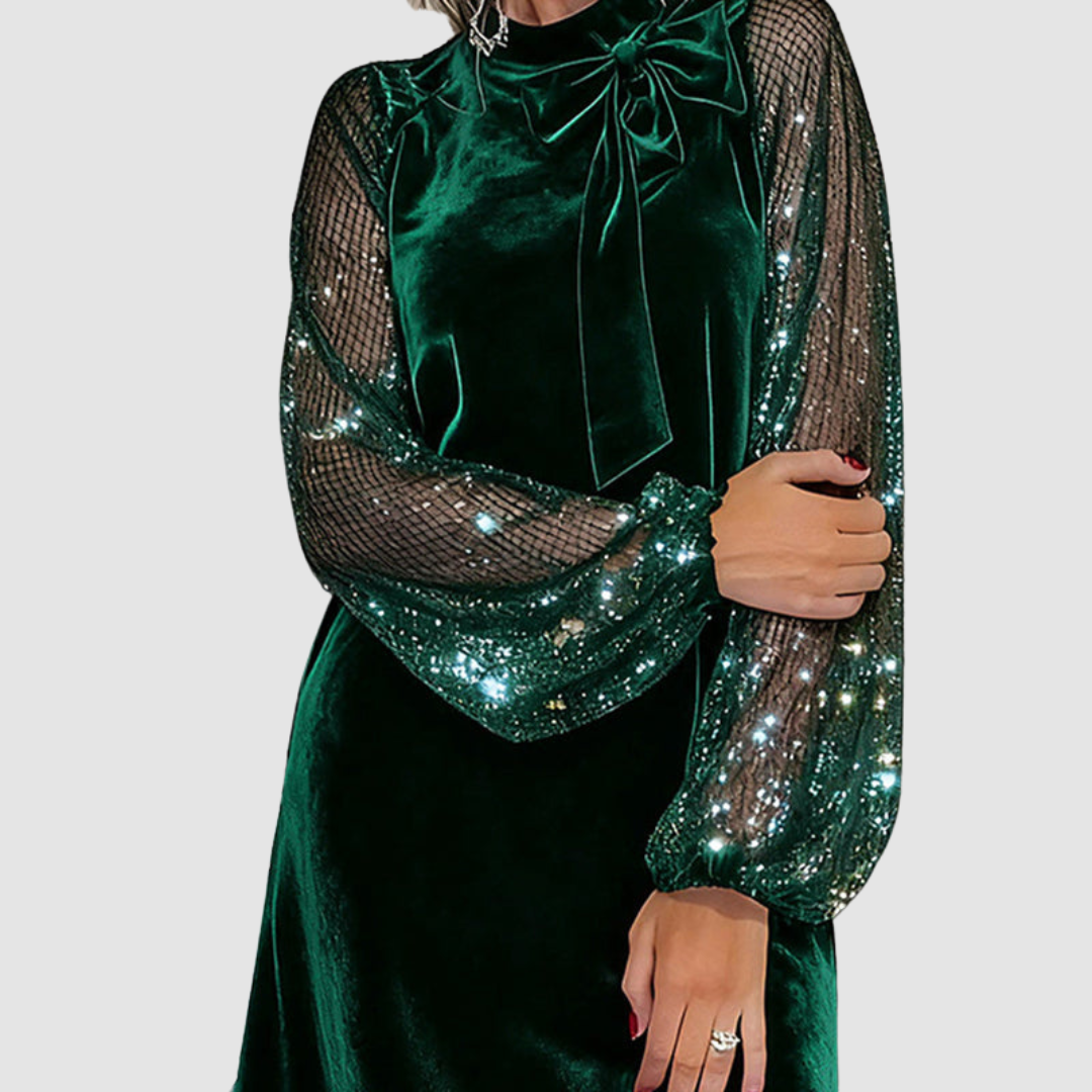 Close-up of green dress with shimmering mesh sleeves and bow detail, worn by a model, on a gray background.