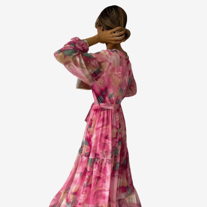 Back view of elegant pink dress featuring vibrant patterns, cinched waist, and long, flowing skirt. Model in studio setting.