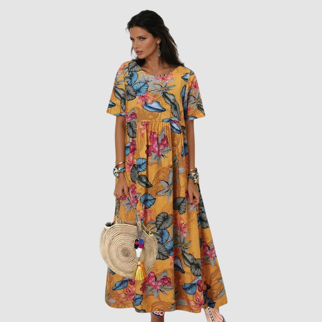 Lady wearing a yellow summer dress with colorful floral print, holding a straw bag, in a neutral studio setting.