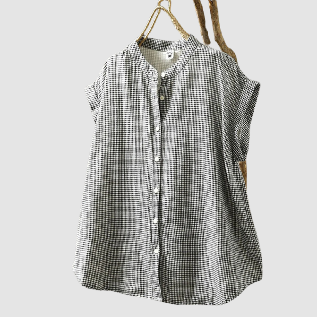 Black and white checkered vintage shirt with short sleeves, hanging on a rustic branch against a gray background.