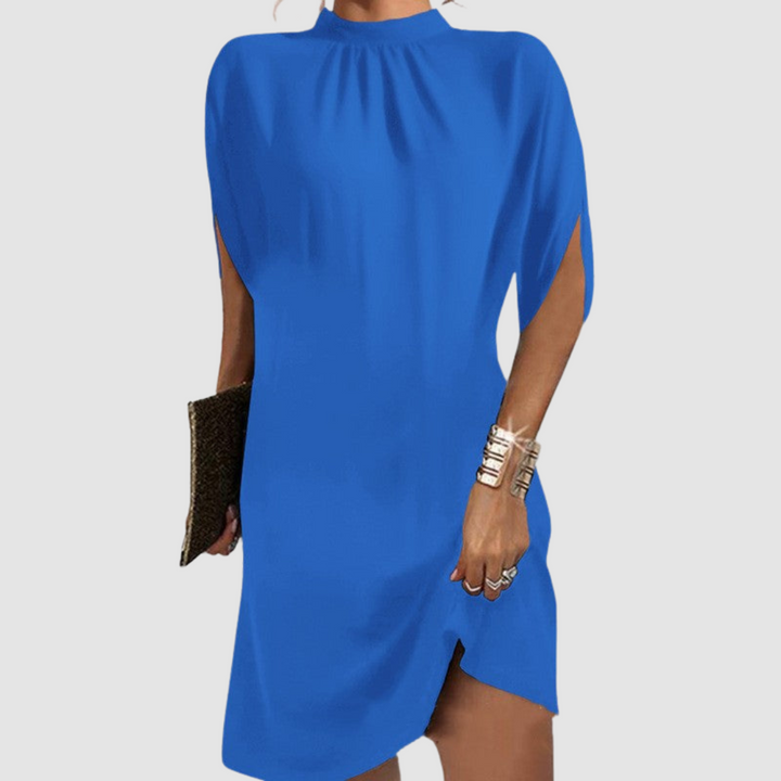 Blue knee-length dress with loose fit and stylish high neck, accessorized with gold bangles and clutch on gray background.