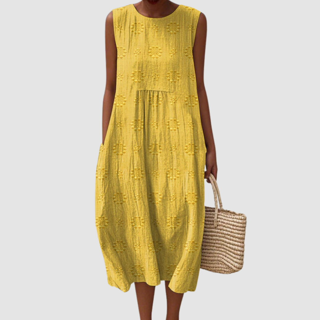Bright yellow sleeveless summer dress with floral patterns, model holding a woven basket, white background.
