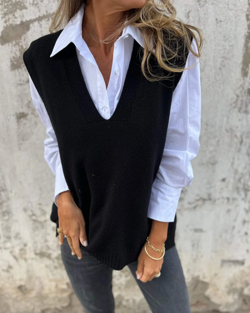 Black knit vest atop a white shirt, modeled by a person beside a worn wall.