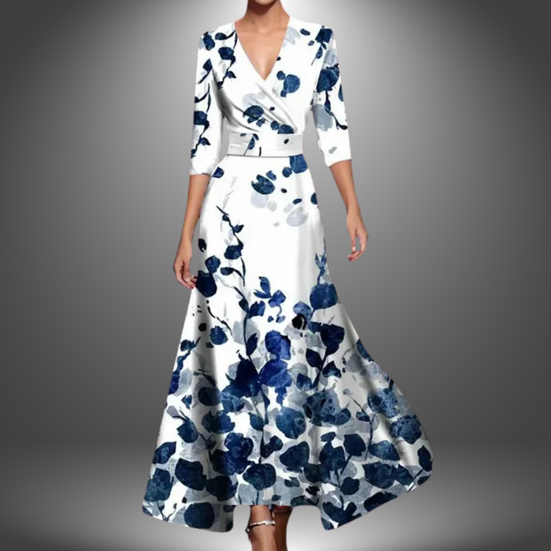 Woman in a long, flowing dress with blue and white floral motif, set against a soft gradient studio backdrop.