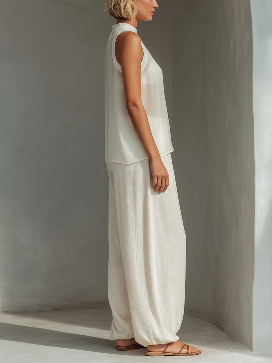 Side profile of model in chic white top and flowing pants, in modern minimalist setting.