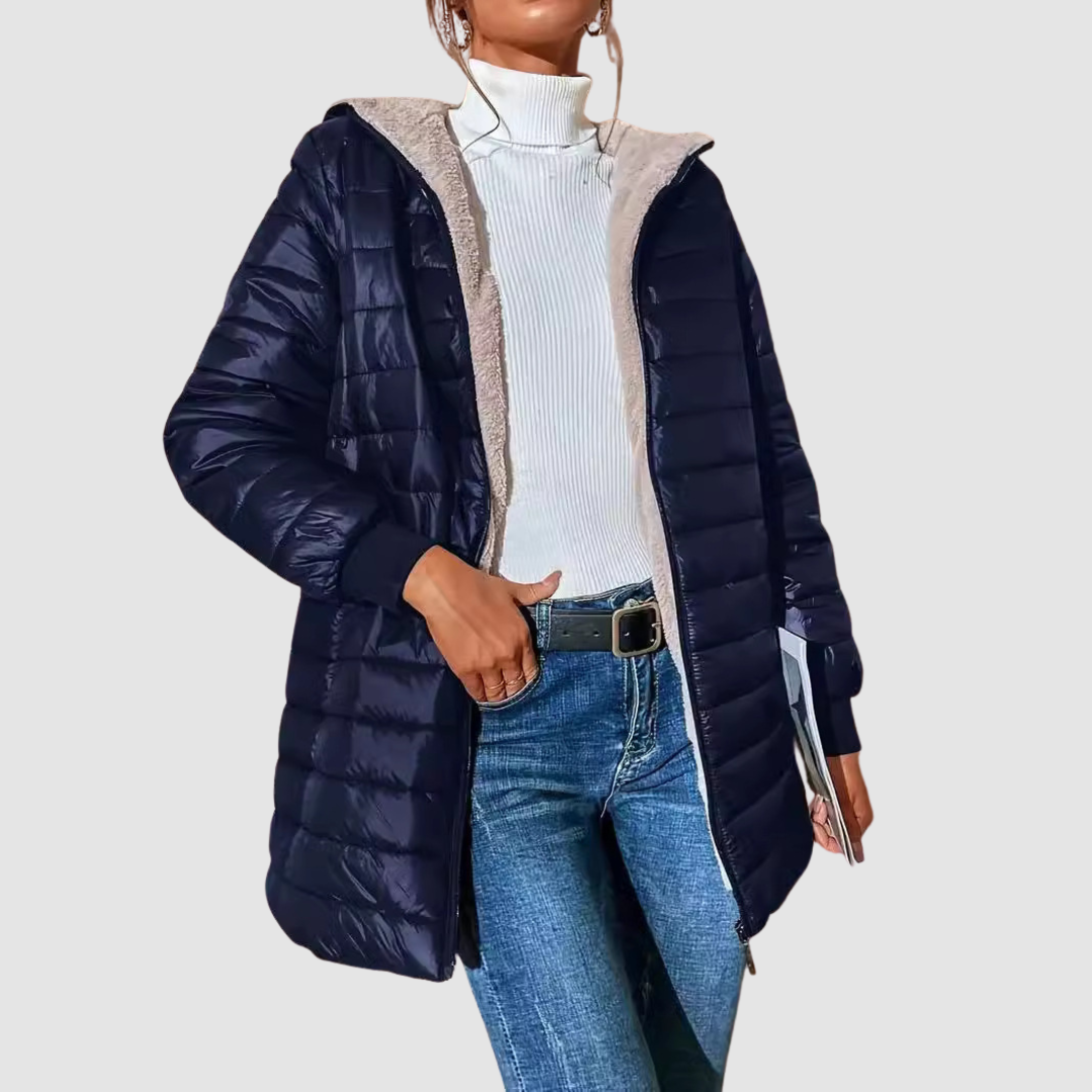 Woman wearing a navy winter coat over a white turtleneck with jeans, holding a book, studio setting.