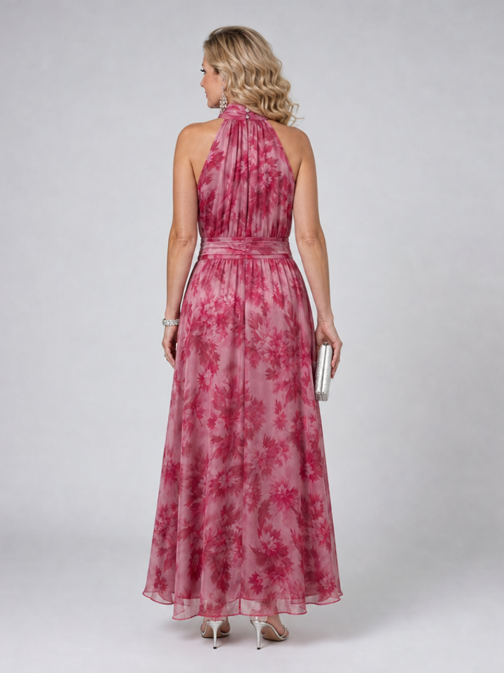 Back view of pink floral halter neck midi dress, woman holding silver clutch, in studio setting.