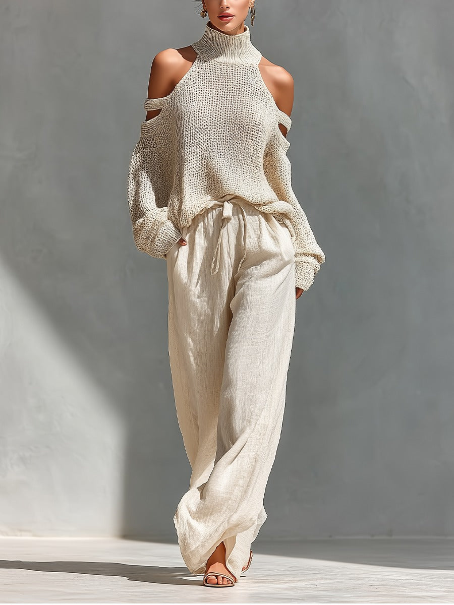 Woman wearing a cream turtleneck sweater with cold shoulder cutouts and flowing cream pants in a sunlit indoor setting.