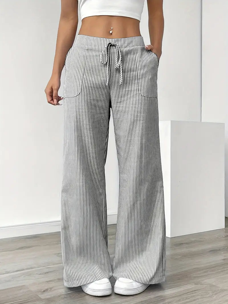 Gray and white striped relaxed pants with drawstring waist, modeled indoors, paired with white sneakers.