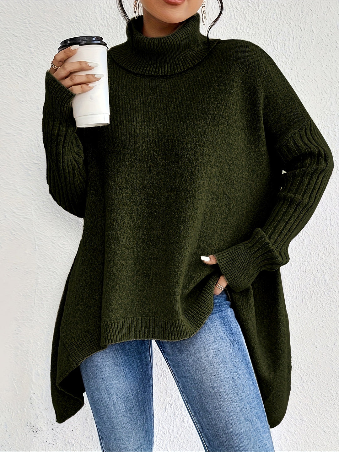 Green turtleneck sweater with long sleeves, holding a coffee cup, paired with jeans against a white background.