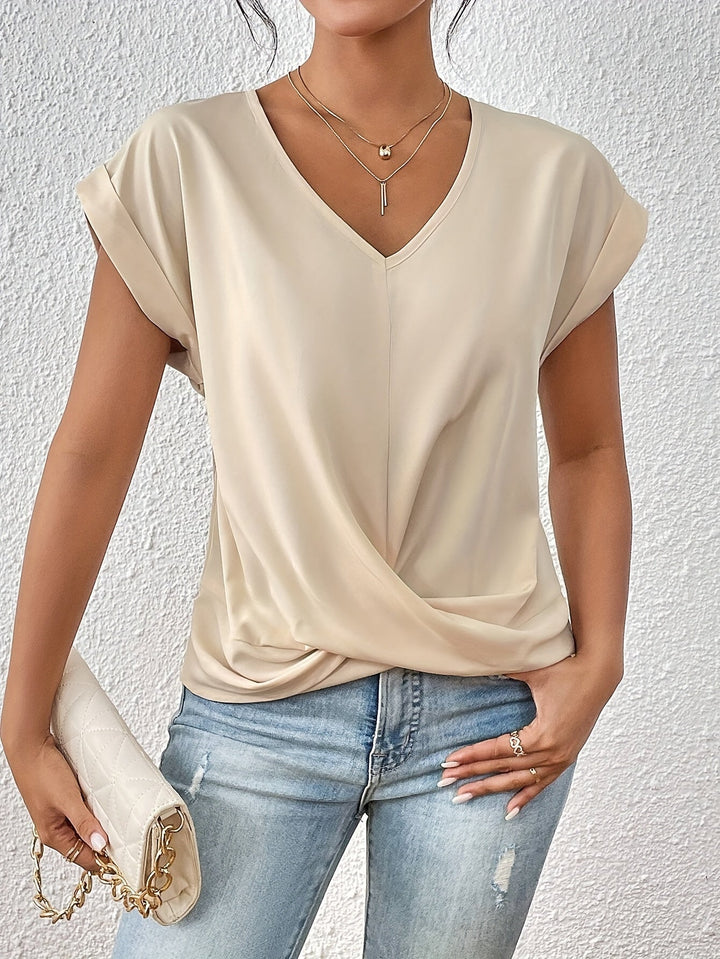 Beige V-neck T-shirt with rolled sleeves, styled with light jeans and a white quilted clutch, against a textured white wall.
