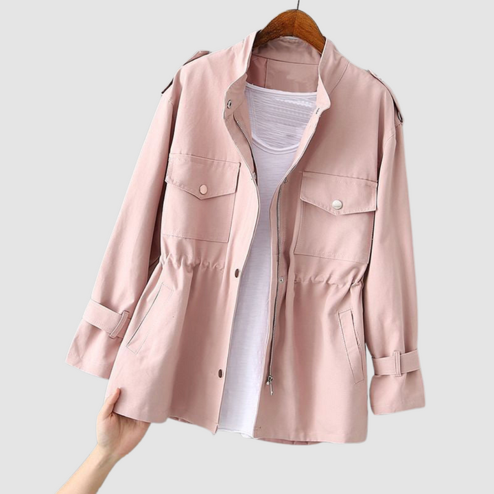 Light pink jacket with front pockets and cinched waist, hanging on a wooden hanger on a white background.