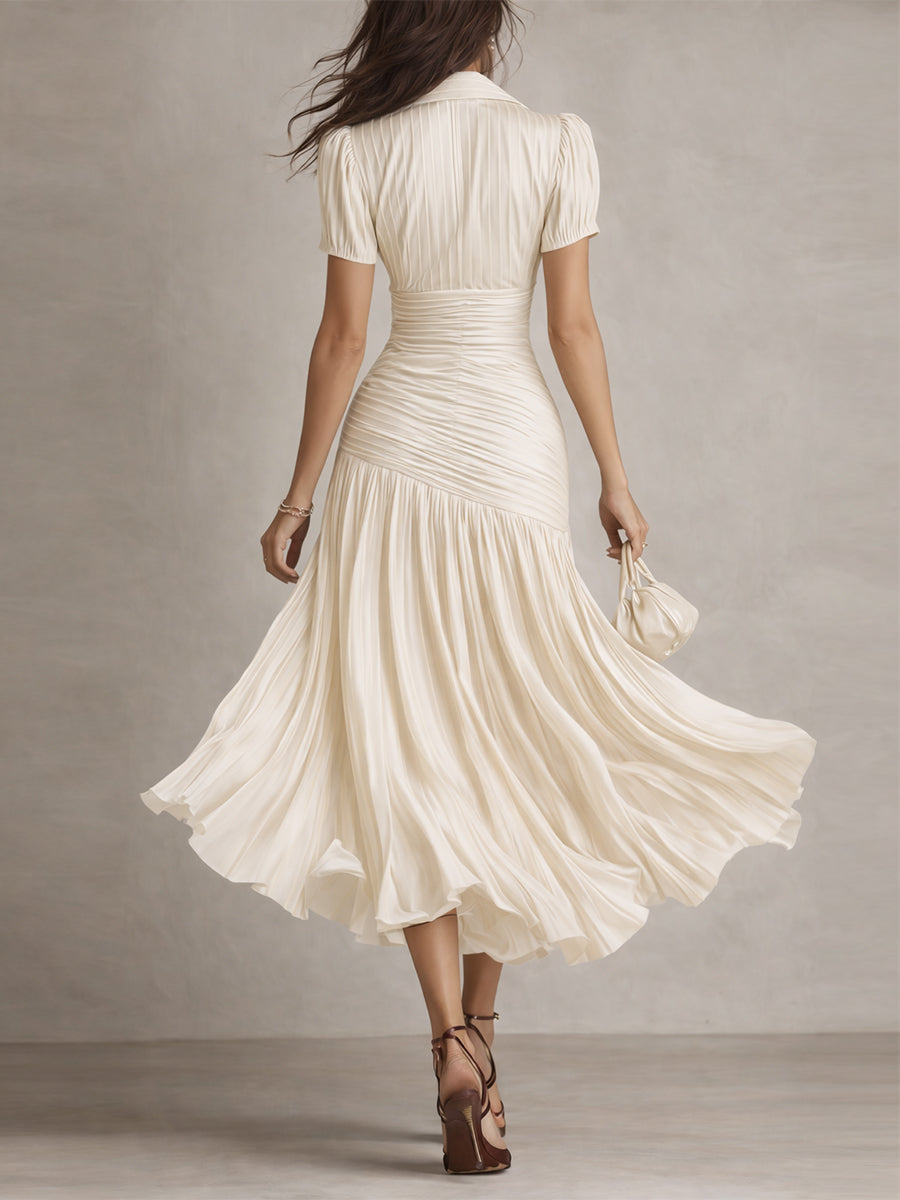 Back view of model in cream midi dress with detailed pleats and short sleeves, walking in a neutral studio.