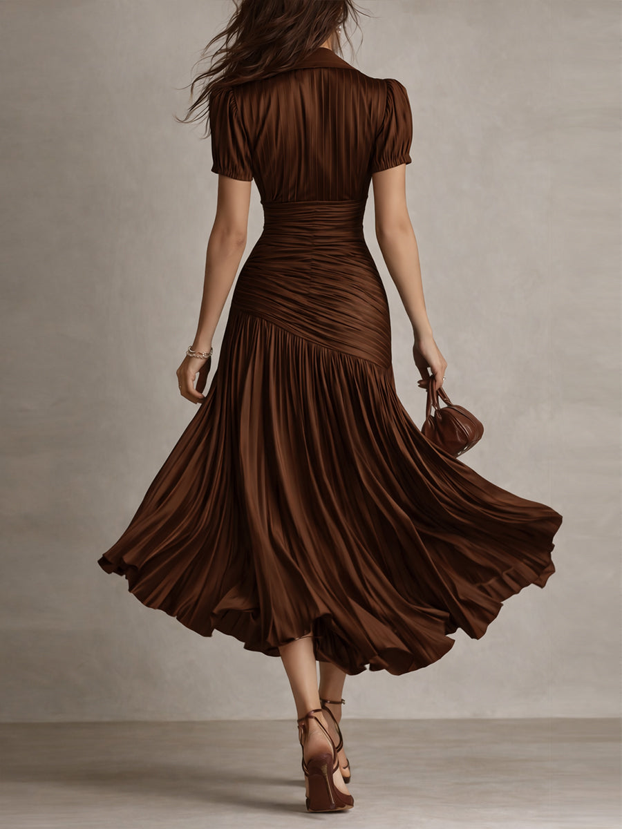 Back view of model in brown midi dress with detailed pleats and short sleeves, walking in a neutral studio.