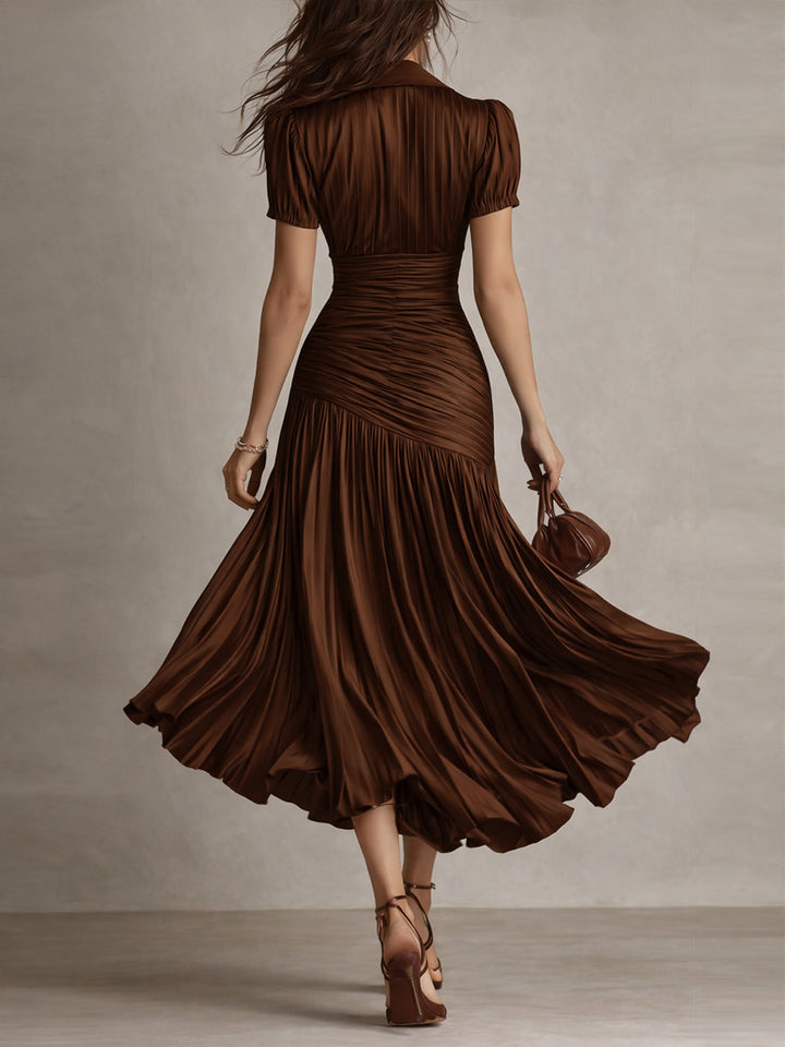 Back view of model in brown midi dress with detailed pleats and short sleeves, walking in a neutral studio.