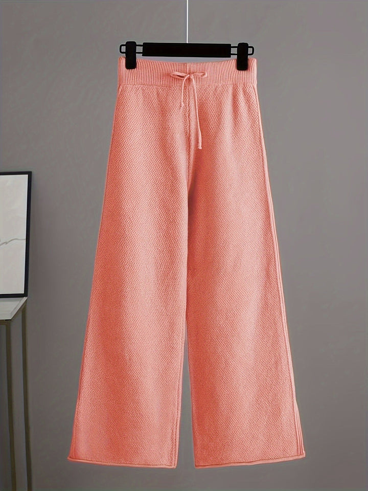 Light pink knit pants featuring a drawstring and loose fit on a hanger, gray background.