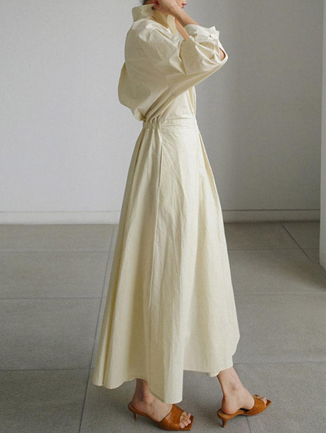 Side view of cream midi dress with button lapel, loose fit, worn indoors with brown sandals.