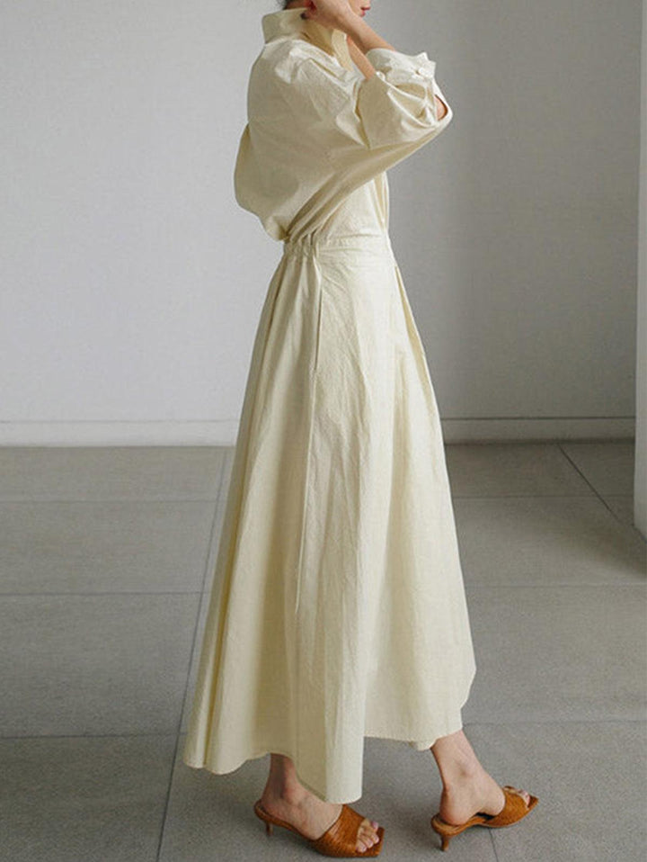 Side view of cream midi dress with button lapel, loose fit, worn indoors with brown sandals.