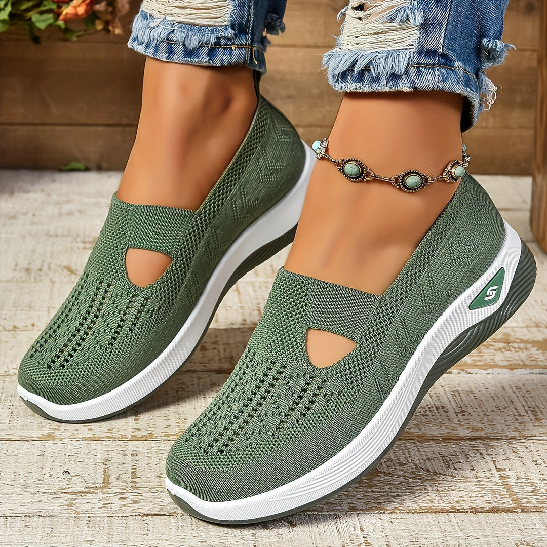 Green non-slip orthopedic shoes worn with anklet, distressed jeans on wooden floor.