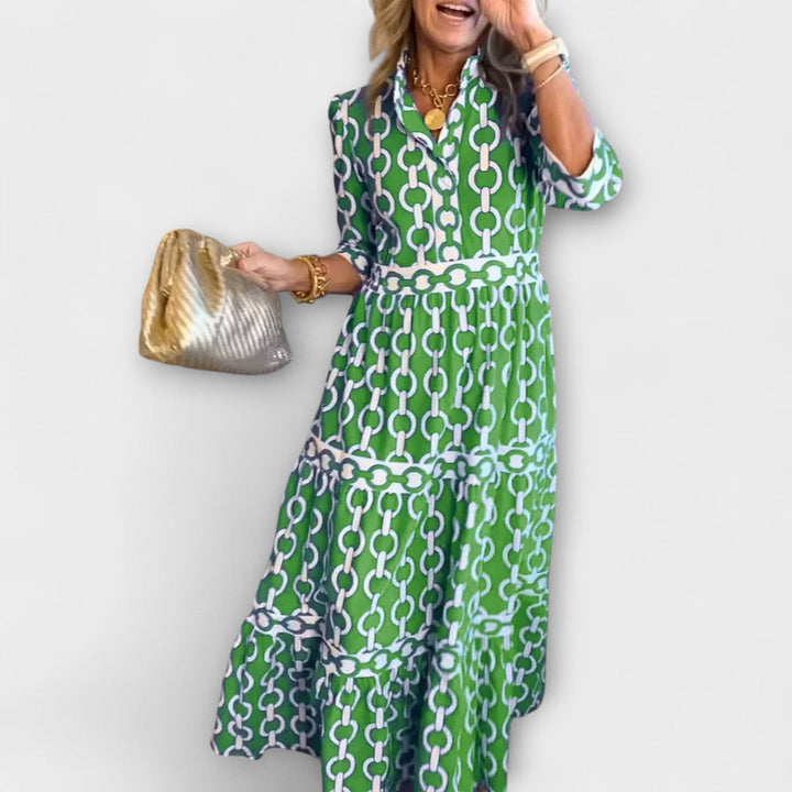 Woman in green and white chain print midi dress holding a gold bag against a plain background.