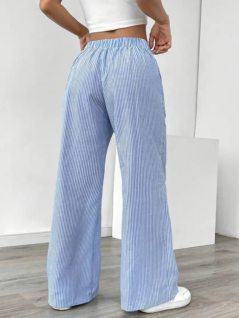 Back view of blue and white striped relaxed pants with elastic waistband, modeled indoors with white sneakers.
