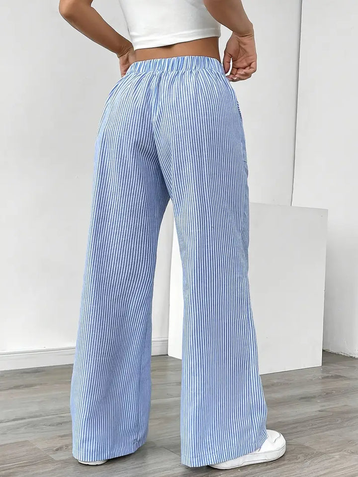 Back view of blue and white striped relaxed pants with elastic waistband, modeled indoors with white sneakers.
