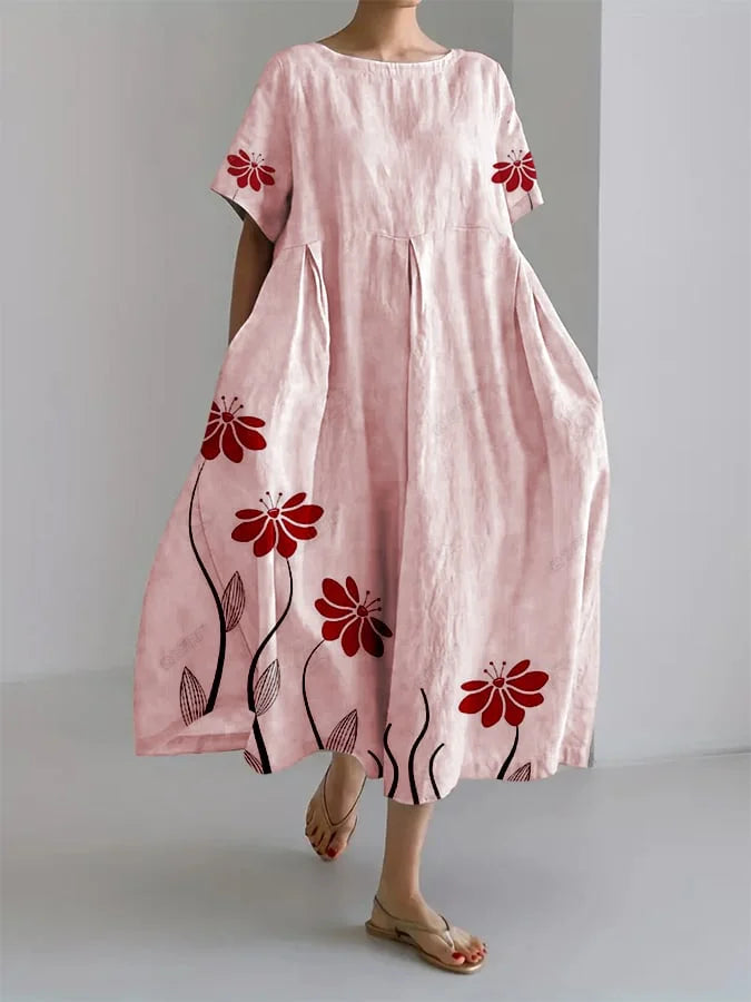 Woman wearing a pink floral summer dress with red flowers, standing in a minimalist indoor setting.
