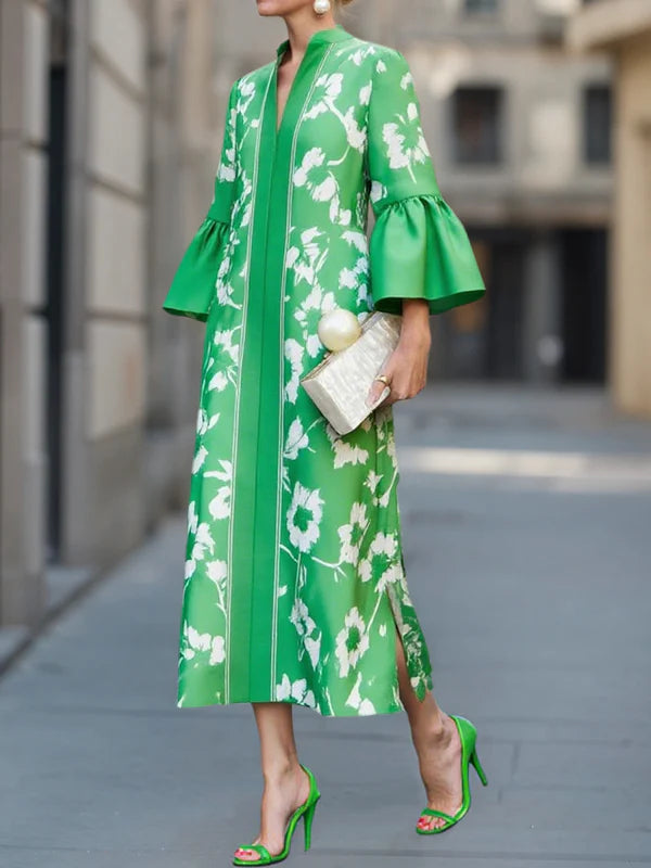 Woman wearing a green floral bell sleeve maxi dress with a deep V-neck, standing outdoors in an urban setting holding a clutch.