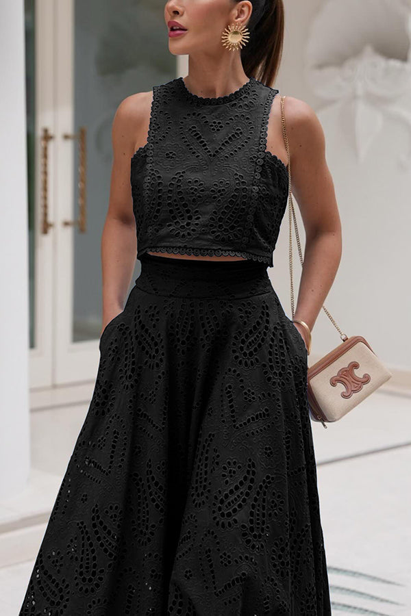 Woman in a black embroidered top and high-waist maxi skirt carrying a small bag in an indoor setting.